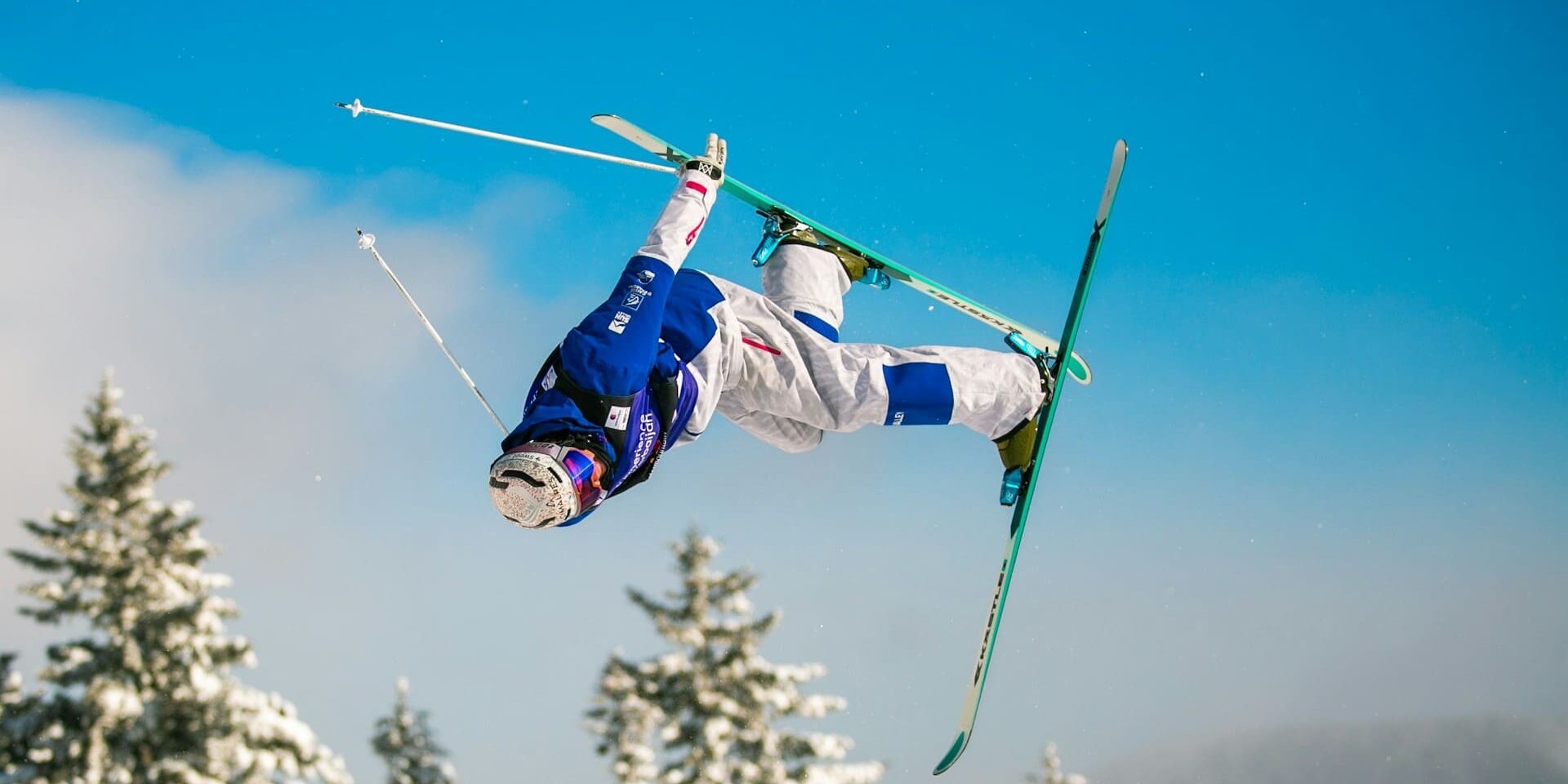 Freestyleskiër in de lucht tijdens acrobatische sprong met blauwe outfit, voorbeeld van fit en voorbereid op wintersport.