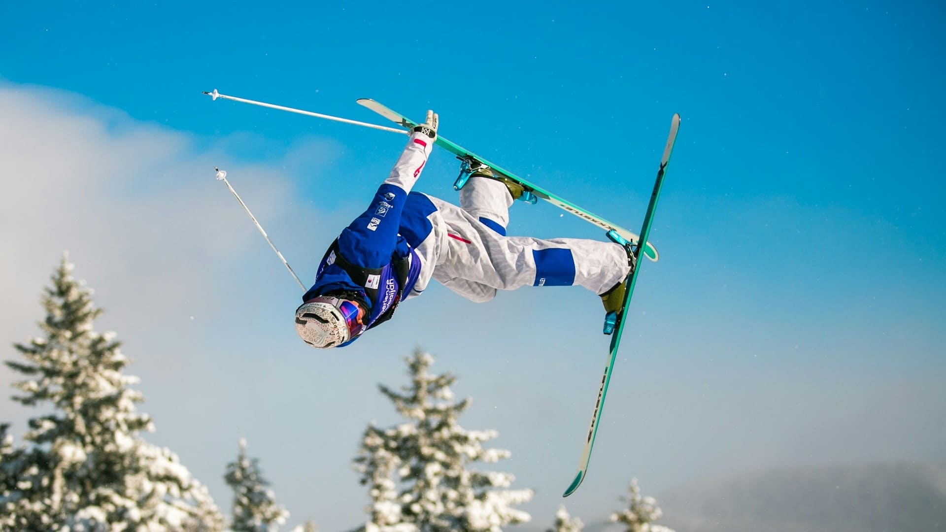 Freestyleskiër in de lucht tijdens acrobatische sprong met blauwe outfit, voorbeeld van fit en voorbereid op wintersport.