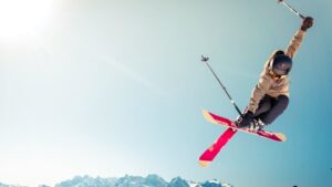 Wintersporter voert een sprong uit met rode ski’s tegen een heldere berglucht, perfect voorbereid voor de wintersport.