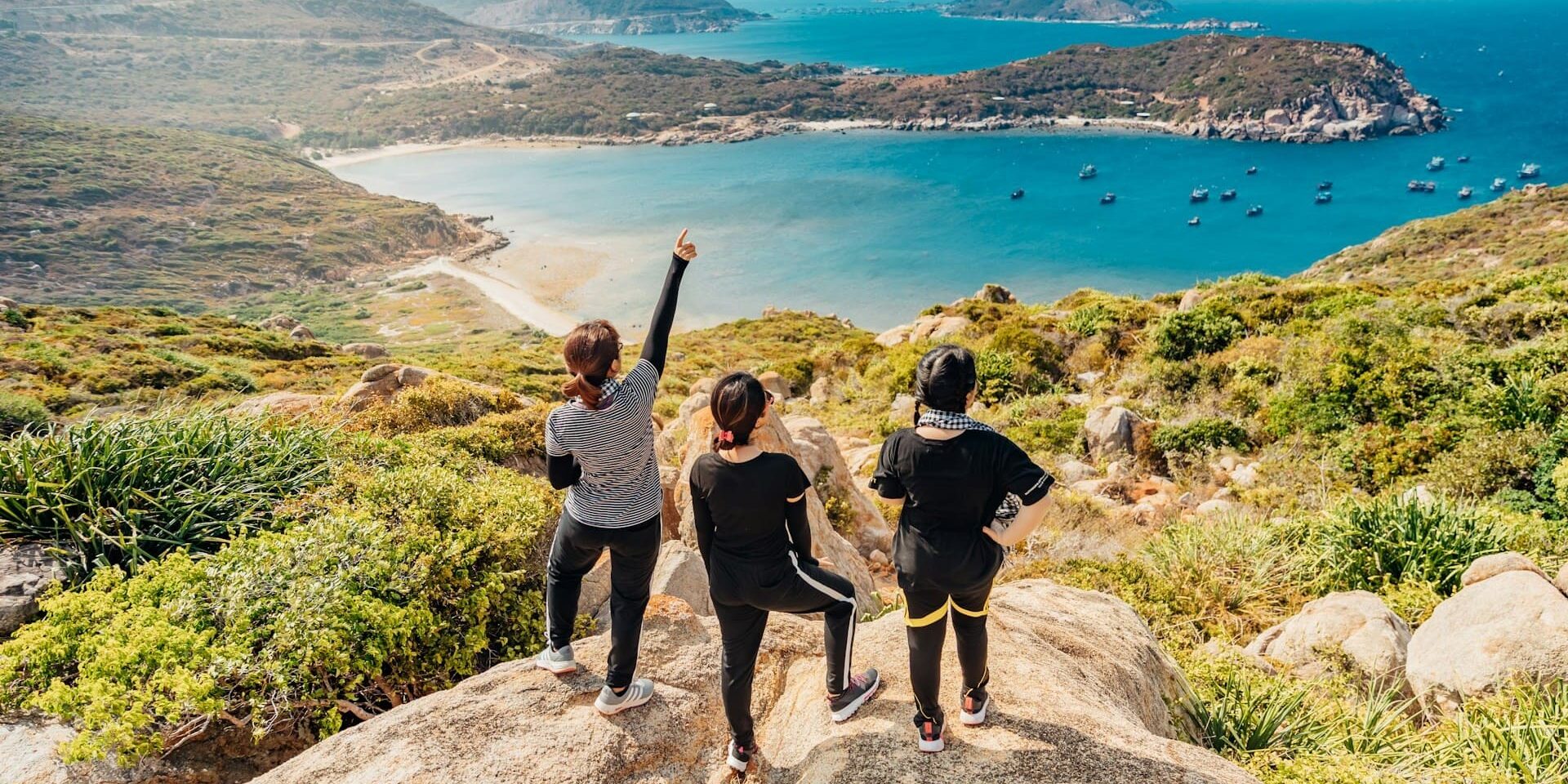 Drie vrouwen wandelen naar uitzichtpunt aan zee tijdens actieve vakantie met leeftijdsgenoten in bergachtig landschap