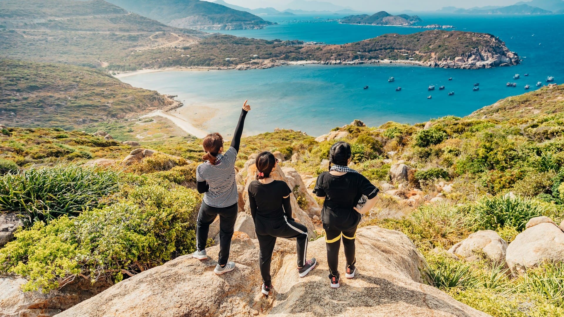 Drie vrouwen wandelen naar uitzichtpunt aan zee tijdens actieve vakantie met leeftijdsgenoten in bergachtig landschap